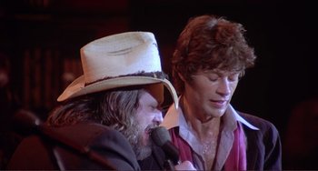 Movie still from “The Last Waltz” (1978), directed by Martin Scorsese – A man in a cowboy hat is singing into a microphone while another man looks on; Close Up shot, Low angle