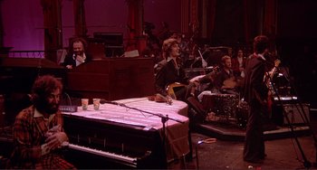 Movie still from “The Last Waltz” (1978), directed by Martin Scorsese – A man sitting at a table in front of an orchestra; Wide shot, High angle