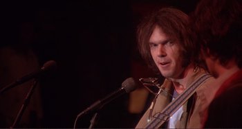 Movie still from “The Last Waltz” (1978), directed by Martin Scorsese – A man holding a guitar and a microphone; Close Up shot, Low angle