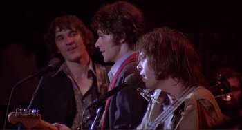 Movie still from “The Last Waltz” (1978), directed by Martin Scorsese – A group of young men standing next to each other on a stage with microphones; Medium shot, Low angle