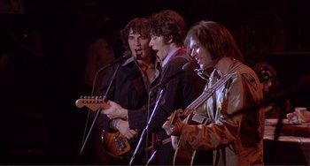 Movie still from “The Last Waltz” (1978), directed by Martin Scorsese – A group of men standing next to each other on a stage with microphones; Medium shot, Low angle