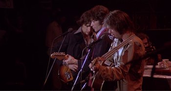 Movie still from “The Last Waltz” (1978), directed by Martin Scorsese – A group of people that are standing around a stage with microphones; Medium shot, Low angle