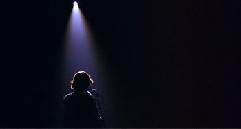 Movie still from “The Last Waltz” (1978), directed by Martin Scorsese – A person standing in front of a microphone on a stage; Wide shot, Low angle