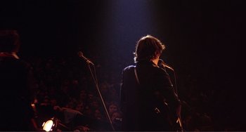 Movie still from “The Last Waltz” (1978), directed by Martin Scorsese – A person standing on a stage with a microphone; Wide shot, Low angle