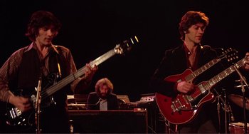 Movie still from “The Last Waltz” (1978), directed by Martin Scorsese – A group of people that are playing a musical instrument together; Medium shot, Low angle
