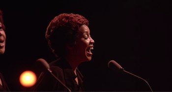Movie still from “The Last Waltz” (1978), directed by Martin Scorsese – A woman with red curly hair standing at a microphone; Medium shot, Low angle