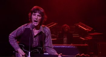 Movie still from “The Last Waltz” (1978), directed by Martin Scorsese – A man is singing into a microphone in front of an audience; Medium shot, Low angle