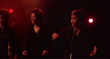 Movie still from “The Last Waltz” (1978), directed by Martin Scorsese – A couple of women standing next to each other on a stage; Medium shot, Low angle