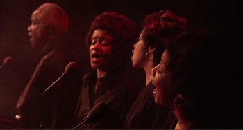 Movie still from “The Last Waltz” (1978), directed by Martin Scorsese – A group of women singing into microphones in a room; Medium shot, High angle