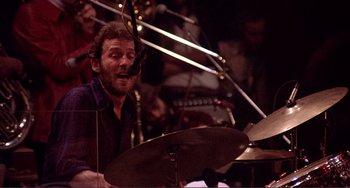 Movie still from “The Last Waltz” (1978), directed by Martin Scorsese – A man playing drums in front of an orchestra; Close Up shot, High angle