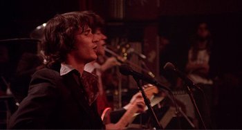 Movie still from “The Last Waltz” (1978), directed by Martin Scorsese – A group of people singing into microphones in a room; Medium shot, Low angle