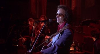 Movie still from “The Last Waltz” (1978), directed by Martin Scorsese – A man in a blue jacket is playing a guitar; Medium shot, Low angle