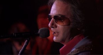 Movie still from “The Last Waltz” (1978), directed by Martin Scorsese – A person wearing sunglasses and a microphone; Close Up shot, Low angle