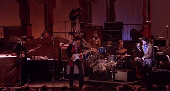 Movie still from “The Last Waltz” (1978), directed by Martin Scorsese – A man playing guitar in front of a group of people; Extreme Wide shot, High angle