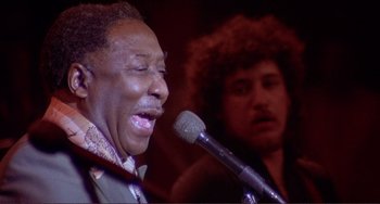 Movie still from “The Last Waltz” (1978), directed by Martin Scorsese – A man singing into a microphone in front of another man; Close Up shot, Low angle