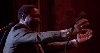 Movie still from “The Last Waltz” (1978), directed by Martin Scorsese – A man holding a microphone in his hand; Medium shot, Low angle