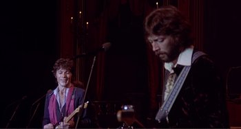 Movie still from “The Last Waltz” (1978), directed by Martin Scorsese – A man playing a guitar and a woman playing a guitar; Medium shot, Low angle