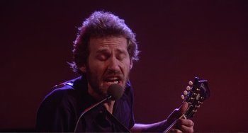 Movie still from “The Last Waltz” (1978), directed by Martin Scorsese – A man with a beard is playing a guitar; Close Up shot, Low angle