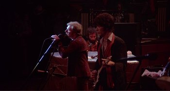 Movie still from “The Last Waltz” (1978), directed by Martin Scorsese – A group of people that are standing in a room together; Medium shot, Low angle