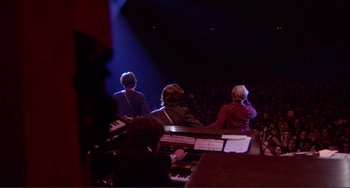 Movie still from “The Last Waltz” (1978), directed by Martin Scorsese – A group of people sitting around a stage with musical instruments; Extreme Wide shot, High angle