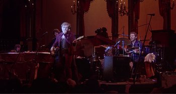Movie still from “The Last Waltz” (1978), directed by Martin Scorsese – A group of people that are performing in a room; Wide shot, Low angle