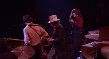 Movie still from “The Last Waltz” (1978), directed by Martin Scorsese – A group of people that are standing up on a stage; Medium shot, Low angle