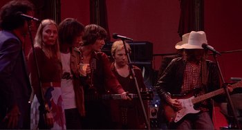 Movie still from “The Last Waltz” (1978), directed by Martin Scorsese – A group of people standing next to each other on a stage; Medium shot, Low angle