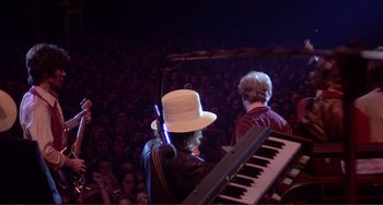 Movie still from “The Last Waltz” (1978), directed by Martin Scorsese – A man wearing a white top hat is playing the piano; Wide shot, Over the shoulder angle