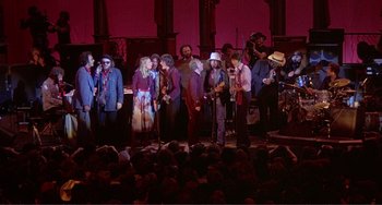 Movie still from “The Last Waltz” (1978), directed by Martin Scorsese – A group of people standing on a stage with microphones; Wide shot, High angle