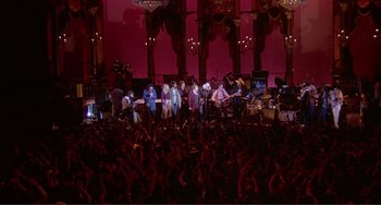 Movie still from “The Last Waltz” (1978), directed by Martin Scorsese – A group of people standing in front of an audience; Extreme Wide shot, High angle