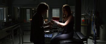 Movie still from “The Lazarus Effect” (2015), directed by David Gelb – Two people sitting in a dark room with one of them holding a bandage; Medium shot, Over the shoulder angle