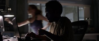Movie still from “The Lazarus Effect” (2015), directed by David Gelb – A man sitting at a table with a woman running in the background; Medium shot, Over the shoulder angle