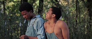 Movie still from “The Learning Tree” (1969), directed by Gordon Parks – Two young men are standing next to each other and laughing; Medium shot, Over the shoulder angle