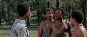 Movie still from “The Learning Tree” (1969), directed by Gordon Parks – A group of young men standing next to each other in a park; Medium shot, Over the shoulder angle