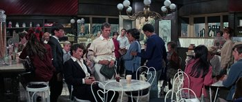 Movie still from “The Learning Tree” (1969), directed by Gordon Parks – A group of people standing around a table in a room; Wide shot, High angle