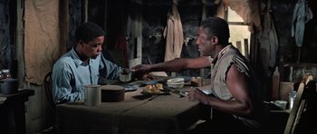 Movie still from “The Learning Tree” (1969), directed by Gordon Parks – Two men sitting at a table with plates of food in front of them; Medium shot, Over the shoulder angle