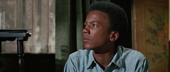 Movie still from “The Learning Tree” (1969), directed by Gordon Parks – A man sitting in front of a window looking off to the side; Close Up shot, Low angle