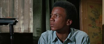 Movie still from “The Learning Tree” (1969), directed by Gordon Parks – A man sitting in front of a window looking off to the side; Close Up shot, Low angle
