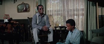 Movie still from “The Learning Tree” (1969), directed by Gordon Parks – A man and a boy sitting on a chair in a living room; Medium shot, Low angle