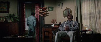 Movie still from “The Learning Tree” (1969), directed by Gordon Parks – A man sitting on a chair in a living room; Wide shot, Low angle