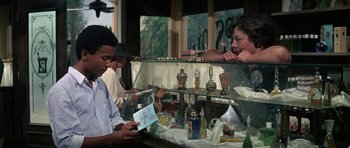 Movie still from “The Learning Tree” (1969), directed by Gordon Parks – A man is looking at a card in a store; Medium shot, Over the shoulder angle