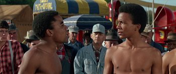 Movie still from “The Learning Tree” (1969), directed by Gordon Parks – Two men face each other in front of a group of people; Medium shot, Low angle