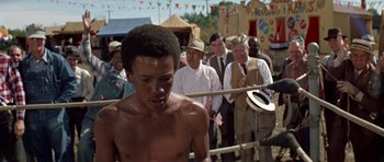 Movie still from “The Learning Tree” (1969), directed by Gordon Parks – A young man is standing in front of a crowd of people; Medium shot, Over the shoulder angle