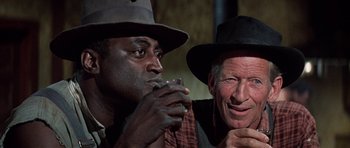Movie still from “The Learning Tree” (1969), directed by Gordon Parks – Two men wearing hats and one is holding a glass of water; Close Up shot, Over the shoulder angle