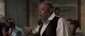Movie still from “The Learning Tree” (1969), directed by Gordon Parks – An older man claps his hands while standing in front of other men; Close Up shot, Low angle