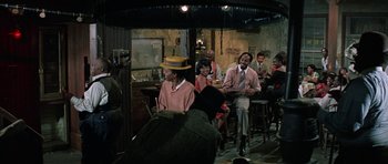 Movie still from “The Learning Tree” (1969), directed by Gordon Parks – A group of people sitting at a table in a room; Wide shot, Over the shoulder angle