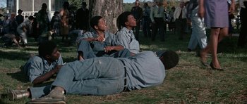 Movie still from “The Learning Tree” (1969), directed by Gordon Parks – Two young men sitting on the ground next to a tree; Medium shot, Low angle
