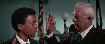 Movie still from “The Learning Tree” (1969), directed by Gordon Parks – Two men in a room one of which is holding his hand up to the other; Medium shot, Over the shoulder angle