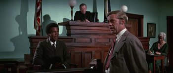 Movie still from “The Learning Tree” (1969), directed by Gordon Parks – Two men in suits and ties in front of a judge in a courtroom; Medium shot, Low angle