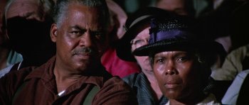 Movie still from “The Learning Tree” (1969), directed by Gordon Parks – A group of people sitting next to each other in a room; Close Up shot, High angle